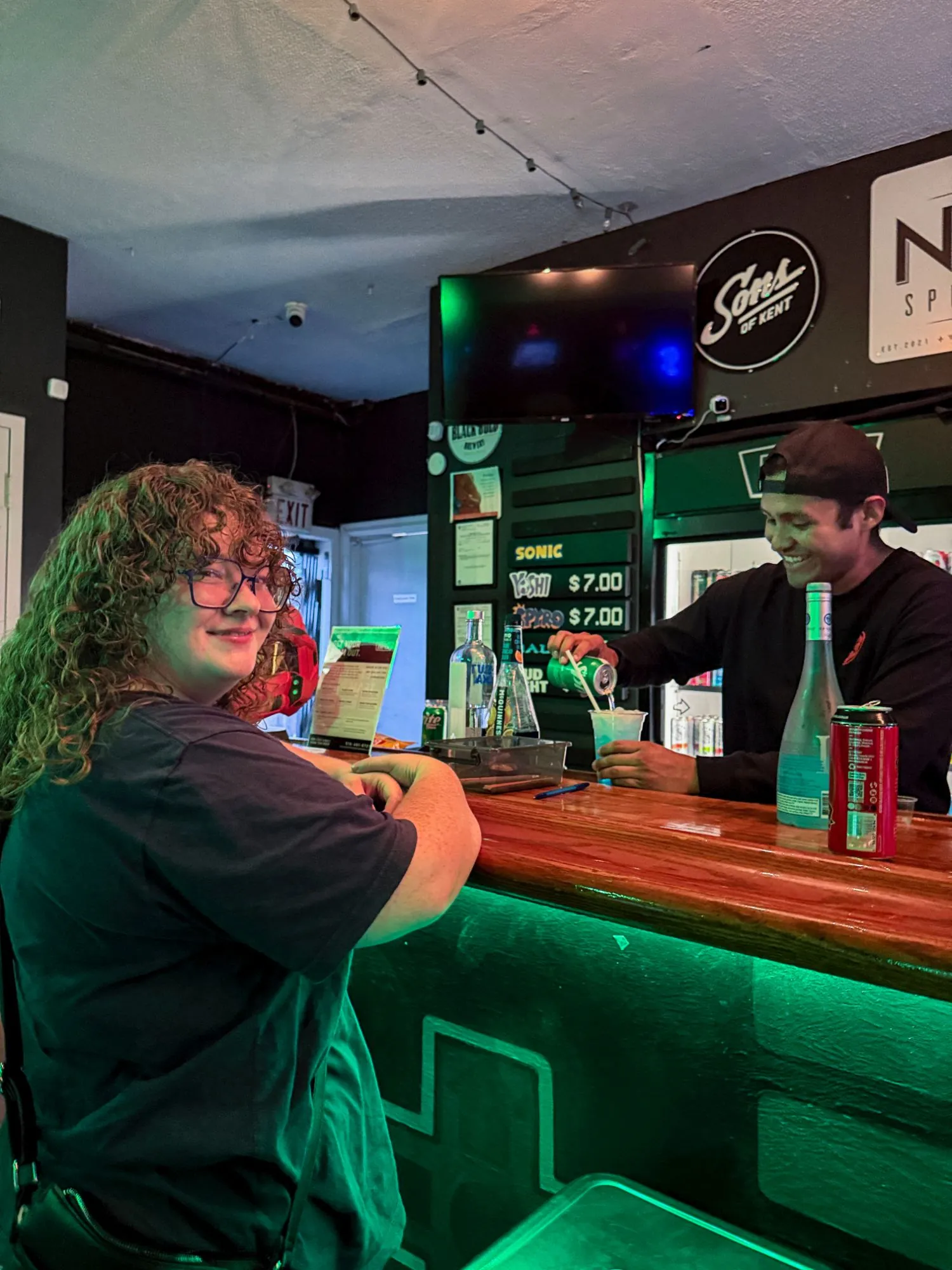 The bartender mixing a drink for a smiling guest at the green-lit bar