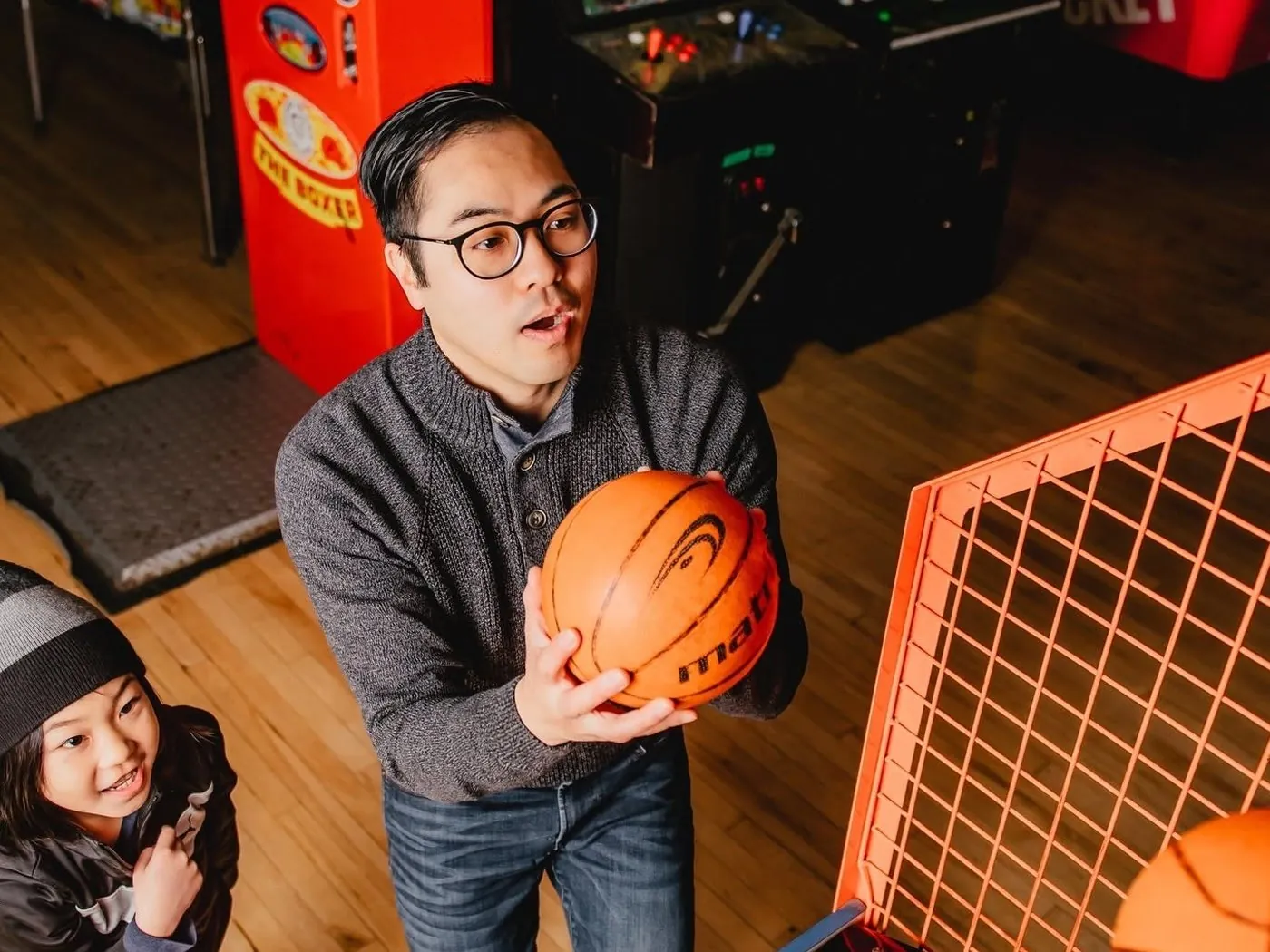 A dad lining up a shot at the basketball game while his kid cheers