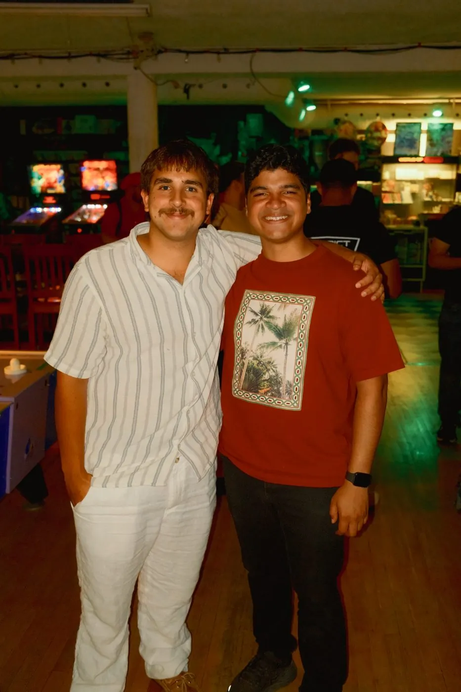 Two friends grinning arm in arm in the arcade