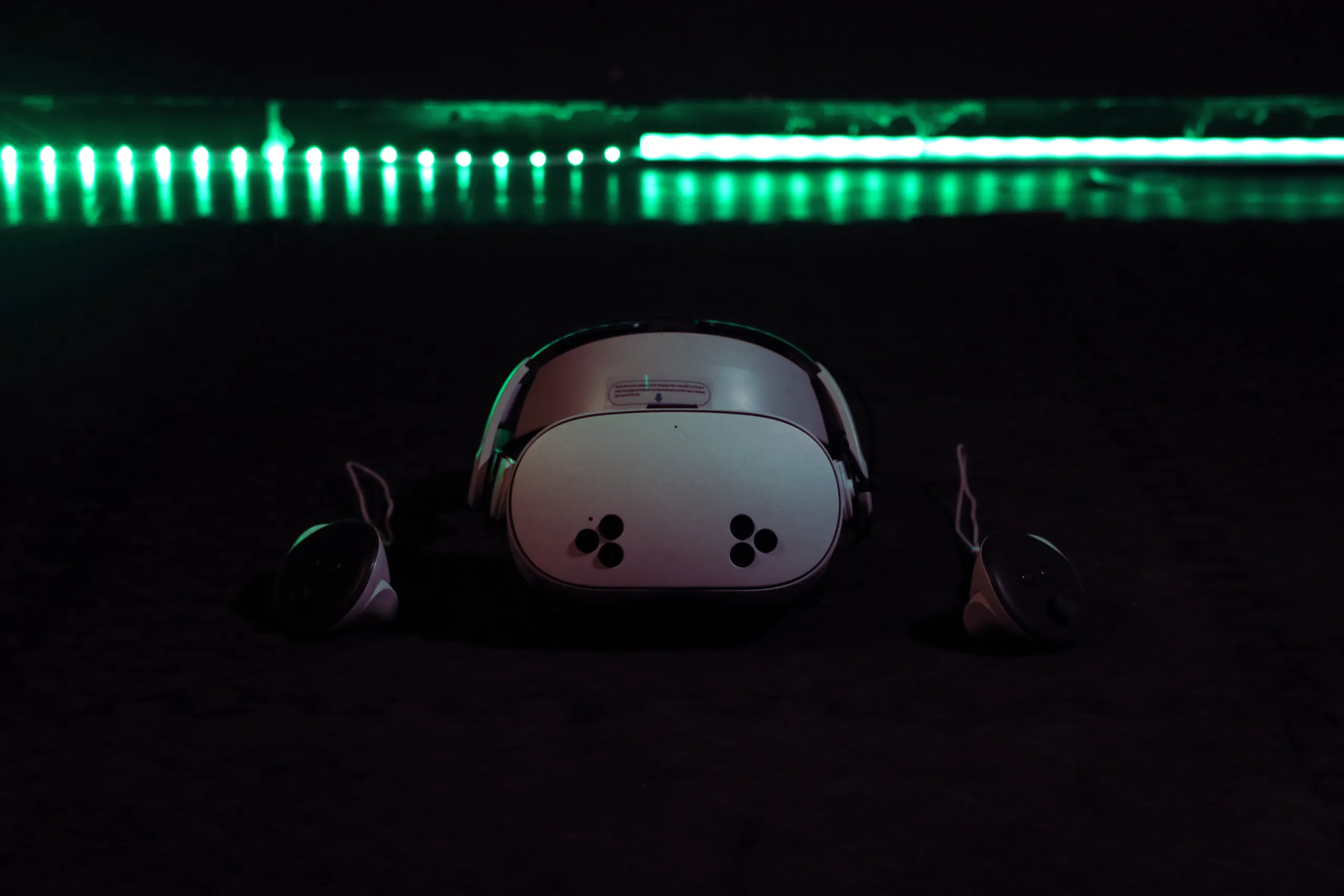 A white VR headset and controllers on the chamber floor under a green light strip