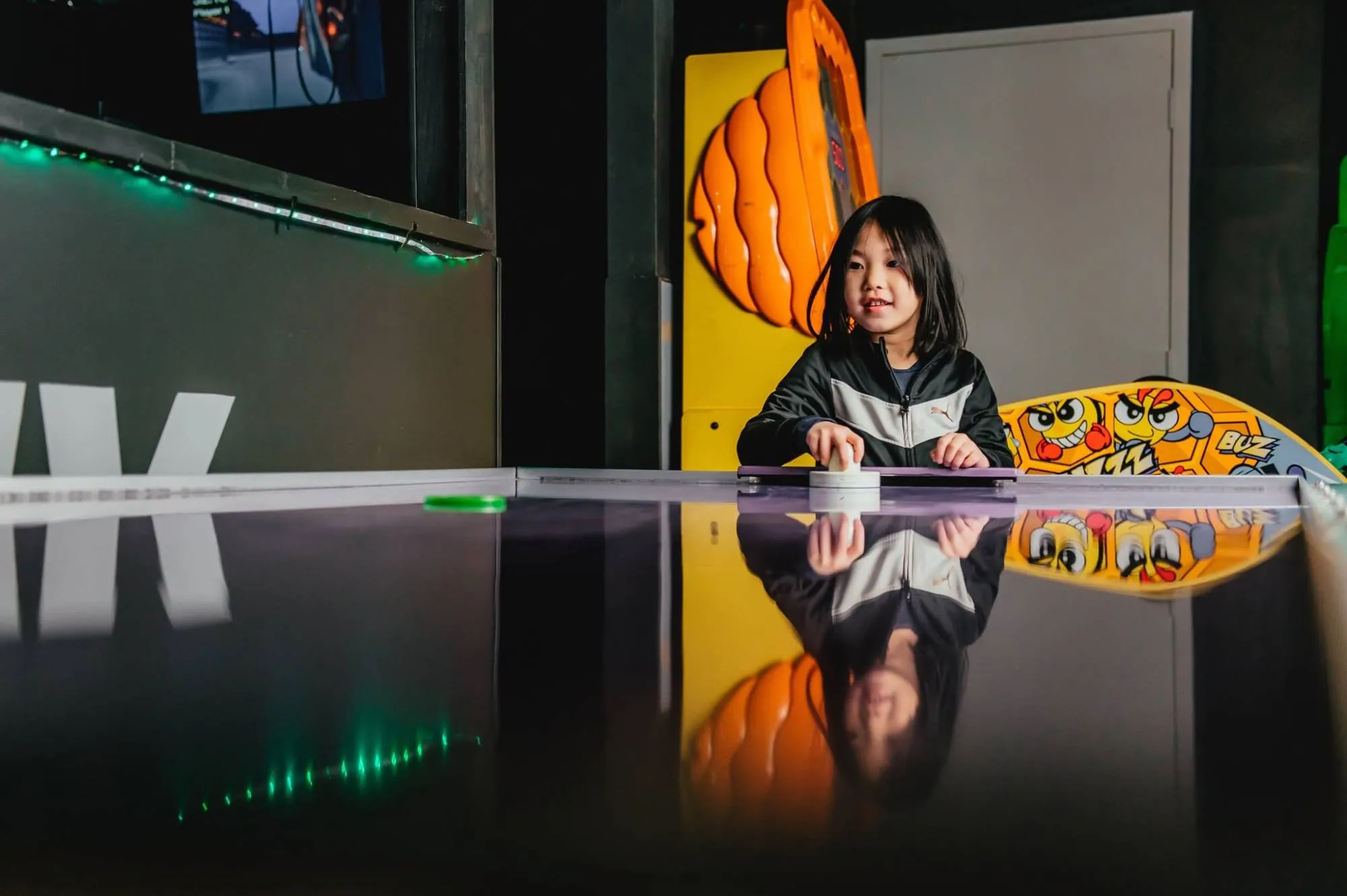 A girl smiling across the air hockey table