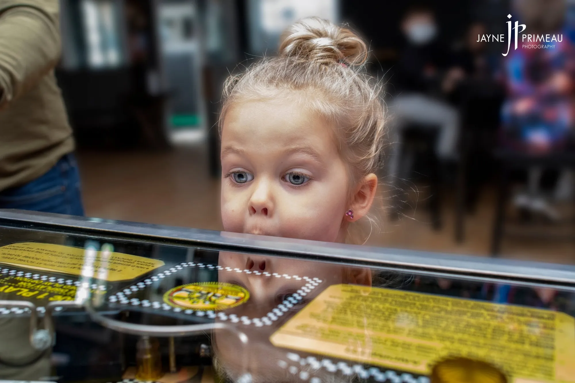 A young girl peering over the glass of a lit-up pinball table