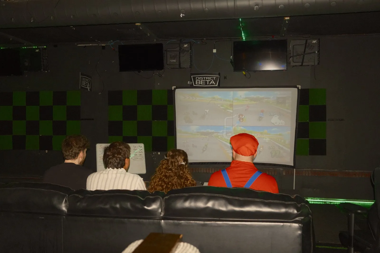 Guests playing Mario Kart on the big screen, one dressed as Mario