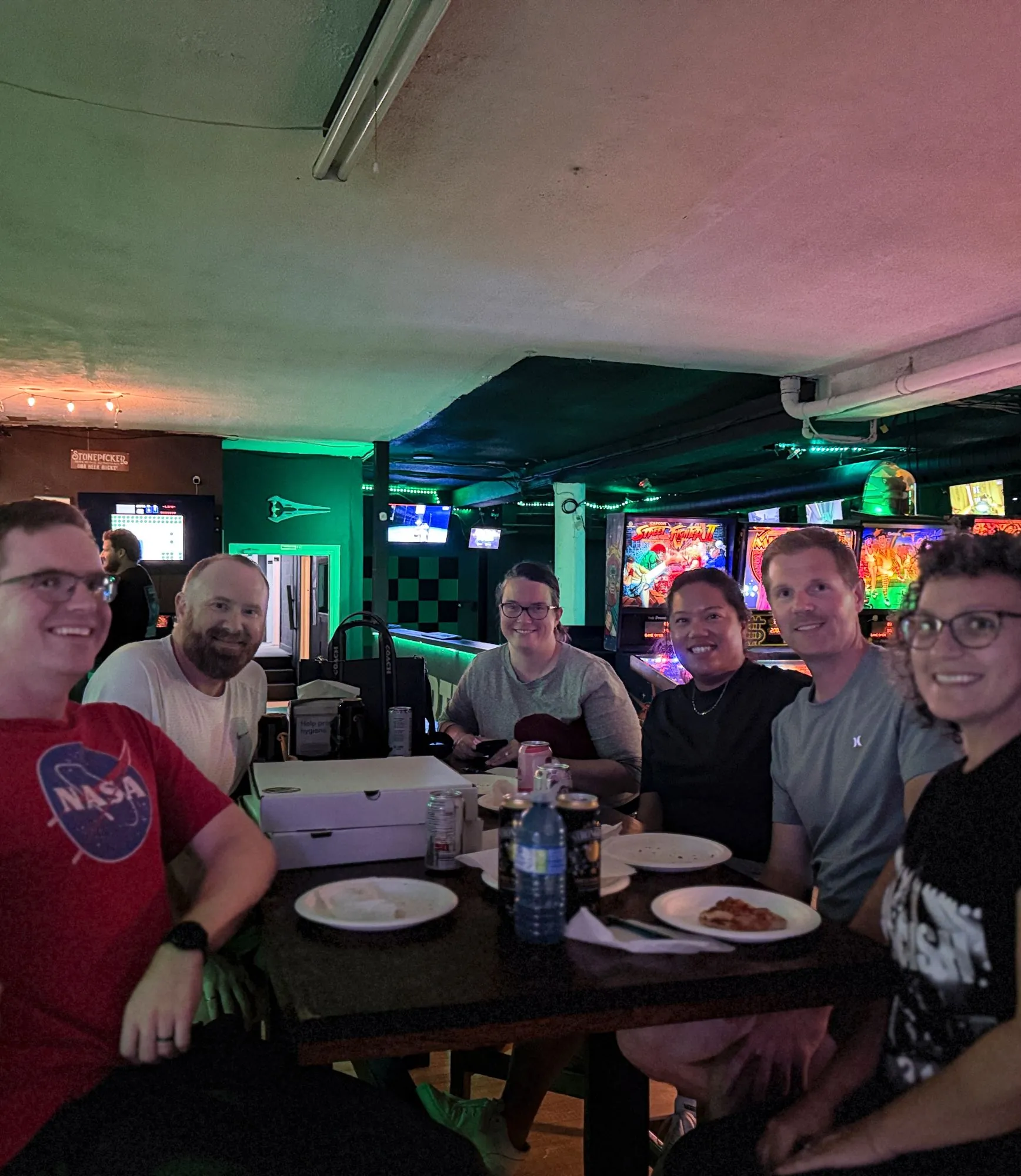 A table of guests with pizza in front of the pinball row
