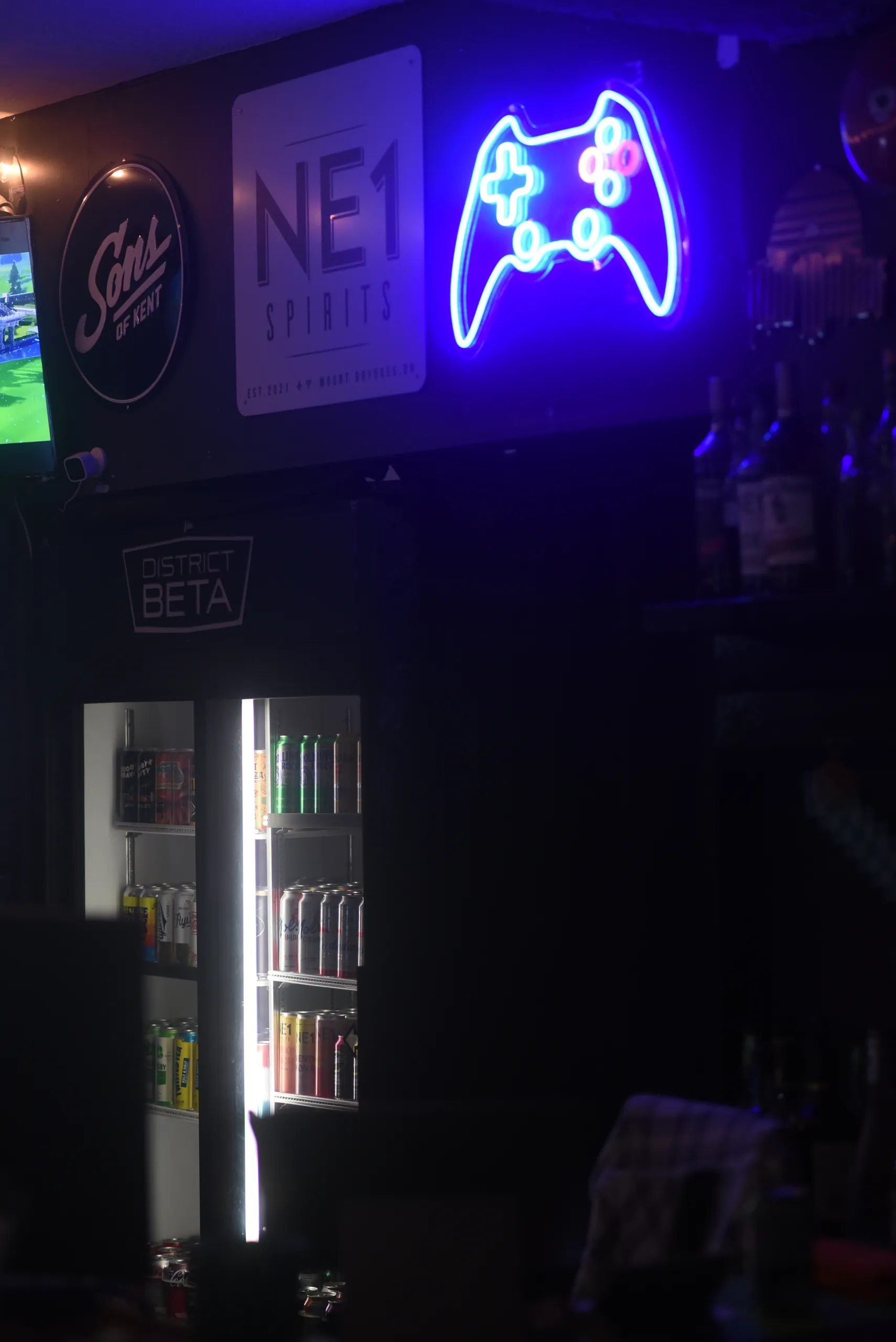 A neon game controller sign glowing over the bar fridge