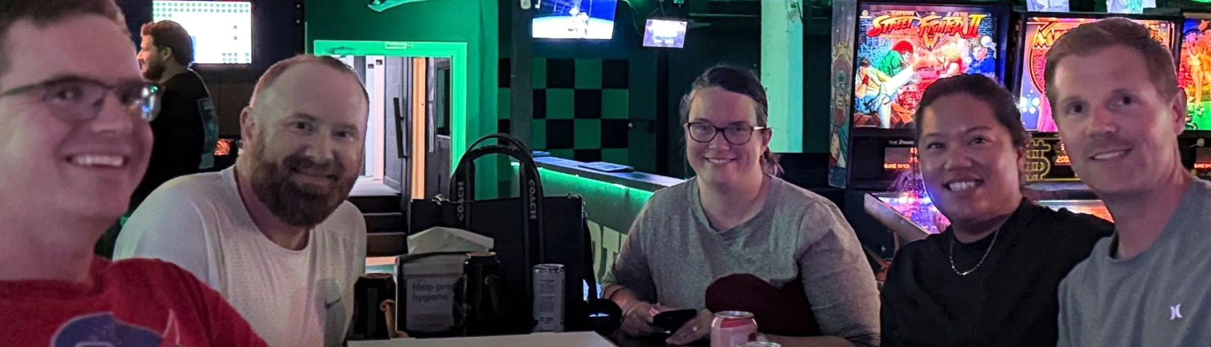 Five coworkers smiling together in the arcade